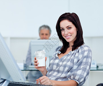 在她的桌子上拿着一个饮料杯的Radiant女商务人士图片