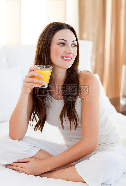 美丽的女人在床上喝橘子汁图片