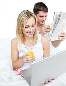 一对夫妇阅读报纸 在床上使用笔记本电脑图片
