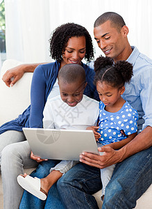 幸福家庭使用笔记本电脑长椅微笑父亲男人夫妻女士沙发技术女孩母亲图片