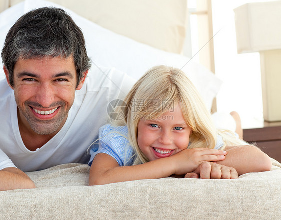 微笑的小女孩与她父亲躺在床上玩得开心图片