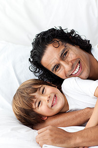 微笑的父亲和他的小儿子躺在床上 在床边微笑图片