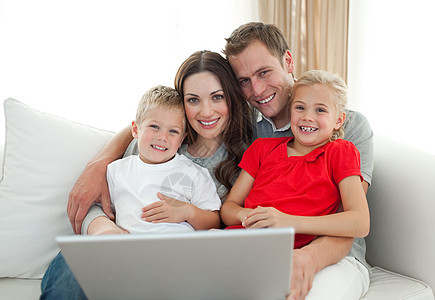 坐在沙发上使用电脑的欢乐家庭图片