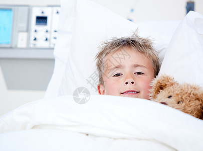 可怜的可爱小男孩躺在医院的床上 带着他的Teddy图片