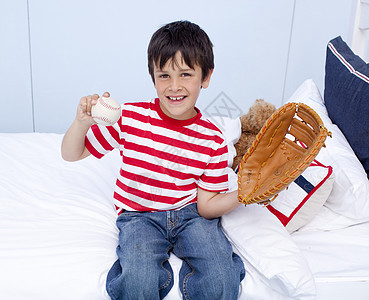 快乐的小男孩在床上打棒球图片