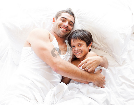 快乐的父亲和儿子看着床上的照相机 看图片