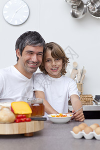 父亲和儿子一起吃早饭乐趣男生橙子家庭父母桌子食物孩子厨房微笑图片