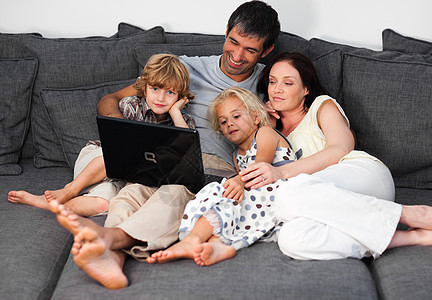 用笔记本电脑在沙发上的年轻家庭图片