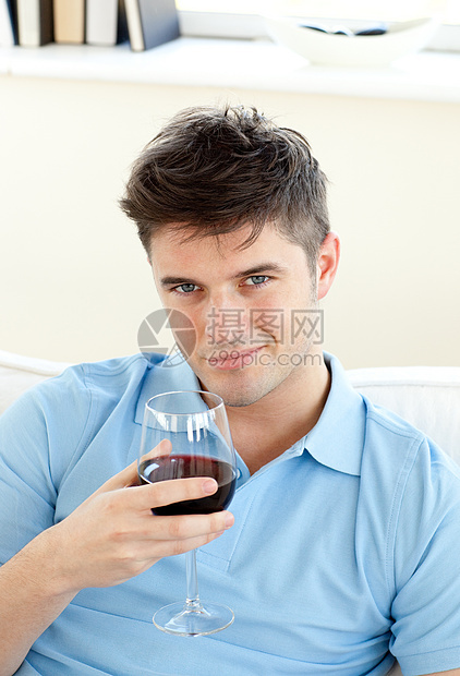 坐在沙发上拿着葡萄酒杯的英俊年轻男子图片
