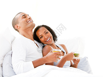 欢快的情侣在床上喝着一杯茶女士拥抱女朋友唤醒饮料男性杯子新婚女性床单图片