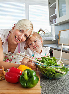 母亲和女儿在厨房准备沙拉时微笑图片