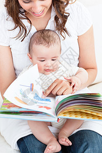 快乐的母亲给坐在沙发上的孩子看一本书图片