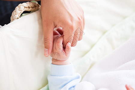 一位年轻母亲紧紧抱着婴儿的手 躺在床上图片