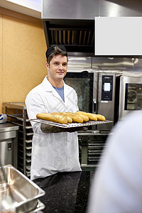 年轻的面包师拿着法棍面包和面包站在厨房里图片