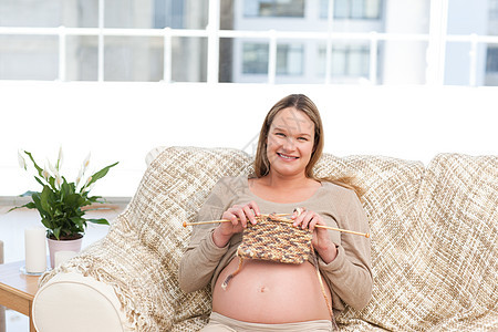 坐在沙发上为未来婴儿编织的漂亮女人图片
