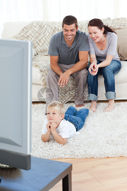 可爱的小男孩和他父母一起看电视在地板上图片