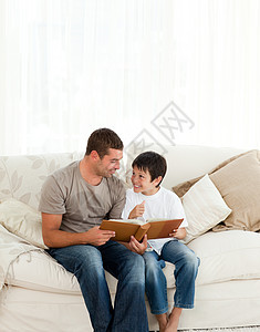 可爱的男孩在看相册时 和他父亲一起坐在沙发上图片
