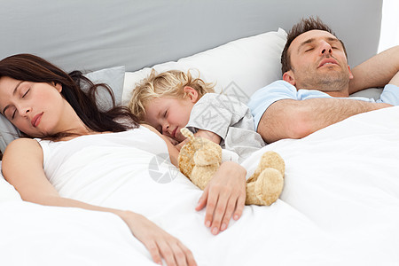 和父母睡在床上的放松的小男孩儿图片