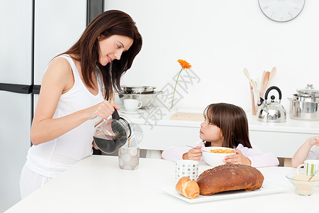 漂亮妈妈在孩子吃早饭时倒咖啡 而她的孩子正在做早餐图片