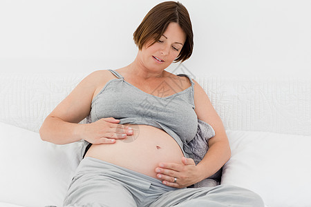 孕妇抱着她的肚子白色婴儿靴子长椅沙发母性成人父母妈妈女性图片