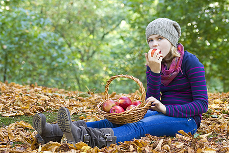 在秋天花园吃红苹果的年轻女孩孩子公园叶子食物衣服花园帽子水果野餐树叶图片