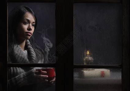 女人在潮湿的窗户后面 喝咖啡或茶图片