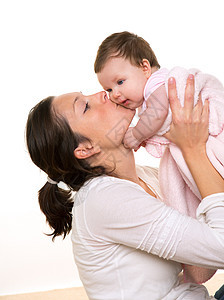 美丽的母亲亲吻女婴时的怀白拥抱快乐婴儿女孩房子后代女士享受母性工作室妻子图片