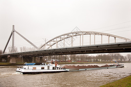 在Holland的桥梁下运输沙子的船只图片