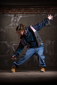 在砖墙上跳现代风格的Hipop舞者霹雳舞街道衣服蓝色黑发牛仔裤运动青少年靴子说唱图片