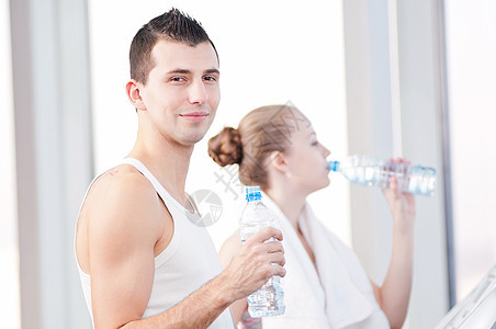 在体育馆运动后饮用饮用水的男女运动装女孩女士教练闲暇中心训练夫妻娱乐健身房图片