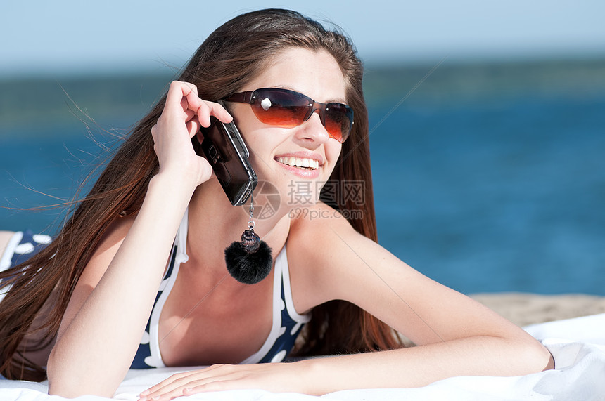 女人在海滩上通过电话聊天乐趣女性游泳衣蓝色女士太阳漫游海岸细胞头发图片