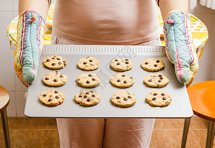 妇女拿着餐盘 用烤饼干和厨房手套食物女士巧克力饼干棕色烤箱早餐托盘小吃芯片图片