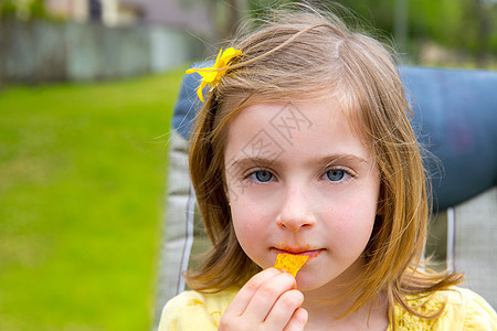 金发女孩在户外公园吃玉米零食眼睛小吃童年金发女郎女性孩子们草地花园蓝色公园图片