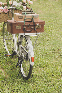田地上的旧式自行车 配有一篮花和袋子草地白色车辆齿轮植物群花园运输车轮花束繁荣图片