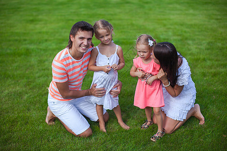 四个四口子的肖像年轻家庭坐在草地上 玩得开心图片