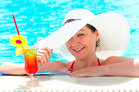 快乐的女孩在游泳池喝鸡尾酒 握着帽子手活动假期边缘果汁闲暇蓝色幸福游客泳池食物图片