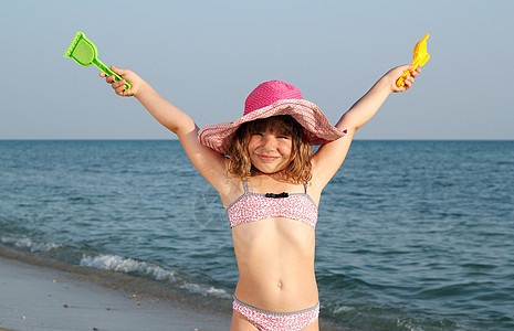 快乐的小女孩 在海滩上举起手女性微笑女儿喜悦帽子闲暇童年假期玩具孩子图片