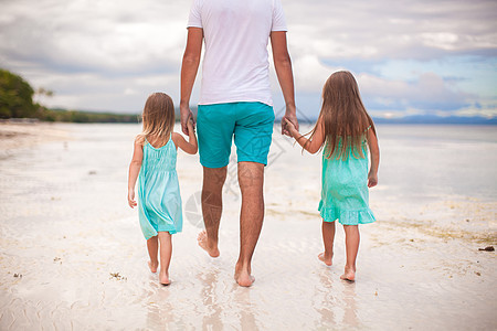 父亲和两个孩子在海边行走的近视图片