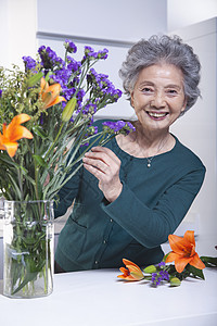 在厨房触摸一包花朵的高级妇女 Portrait图片