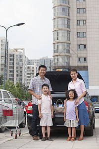 家庭站在汽车旁边 装着购物袋四个人母亲长发冒险休闲家庭服装饮料团结摄影图片