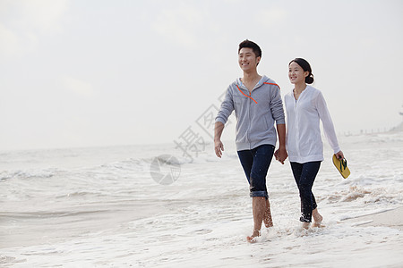 年轻夫妇在中国海滨水边走过中国冲浪假期年轻人旅游女性幸福休闲赤脚天空旅行图片