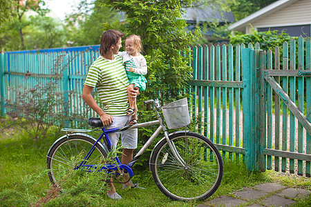 年幼的父亲和可爱的小女儿 在农舍周围骑自行车成人活动骑术微笑父母闲暇家庭爸爸女孩运动图片