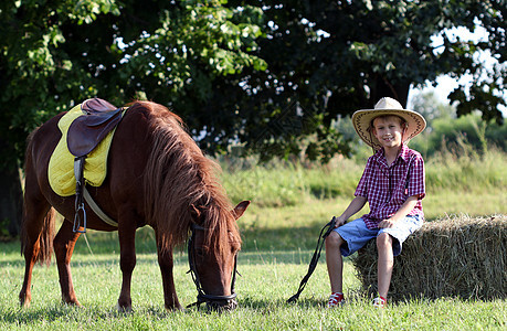 带着牛仔帽和马匹的男孩在农场上图片