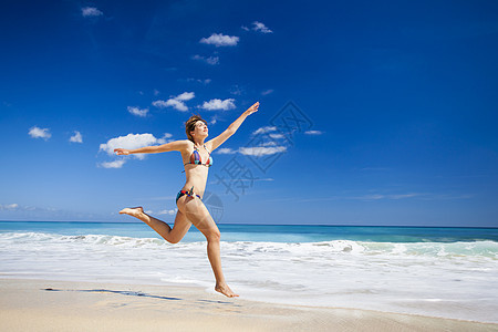 女人在海滩上跳跃女孩旅行蓝色游泳衣比基尼太阳海洋成人天堂跑步图片