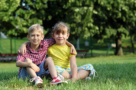 快乐的小女孩和男孩坐在草地上图片