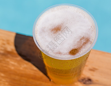 一次性塑料杯中的金啤酒或啤酒边缘安全酒精桌子液体塑料杯子木头泳池气泡图片