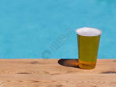 一次性塑料杯中的金啤酒或啤酒泳池桌子草稿酒精安全木头边缘塑料码头丢弃图片