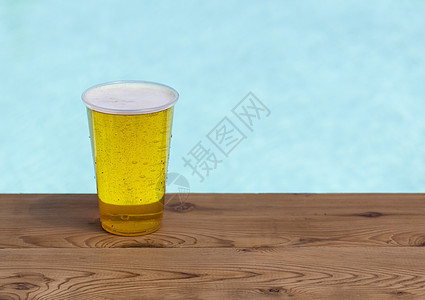 一次性塑料杯中的金啤酒或啤酒玻璃木头码头游泳池泡沫气泡安全派对酒精边缘图片