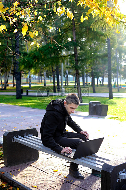 带有膝上型电脑的人长椅公园外套工作小路树木阳光工具男性叶子图片