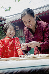 母亲和女儿在传统服装中做面子文化孩子棕色幸福马尾辫微笑乐趣女孩们面团团结图片